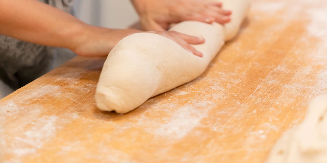 Manos formando una barra de pan sobre la mesa enharinada del obrador